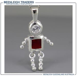 May include: A silver robot pendant with a clear, round gem on the head and a square, red gem for the body. The robot has small, round arms and legs. The pendant hangs from a silver chain.