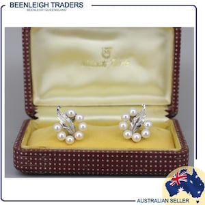 May include: A pair of silver earrings with a floral design and white pearls. The earrings are in a red and gold jewelry box.