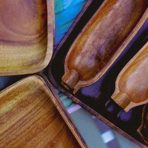 May include: Four wooden serving dishes, two are rectangular and two are long and narrow. The dishes are made of dark brown wood with a natural grain pattern. The dishes are arranged on a blue and purple patterned surface.