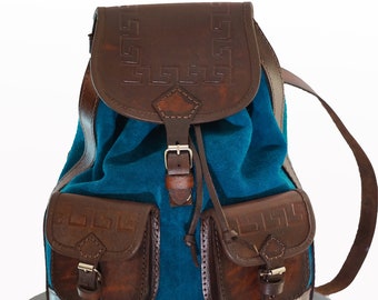 May include: A brown leather backpack with a teal blue suede front panel. The backpack has two front pockets with leather flaps and buckles. The leather has a decorative embossed pattern.