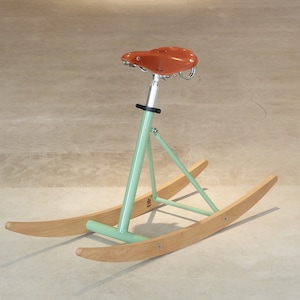 Könnte beinhalten: Ein origineller Schaukelstuhl mit einem Fahrradsattel. Der Sattel ist aus braunem Leder und das Gestell aus hellgrünem Metall. Die Kufen sind aus hellem Holz. Eine kreative Mischung aus Fahrrad und Schaukelstuhl.