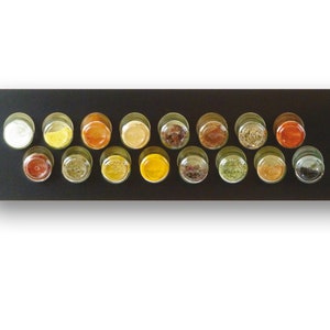 May include: A black spice rack with 16 clear glass jars filled with various spices. The jars are arranged in two rows of eight, each containing a different spice, creating a colorful display. The rack is rectangular with rounded corners.