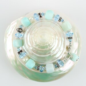 May include: A light blue and silver bracelet with aqua and clear crystal beads. The bracelet is on a white seashell background.