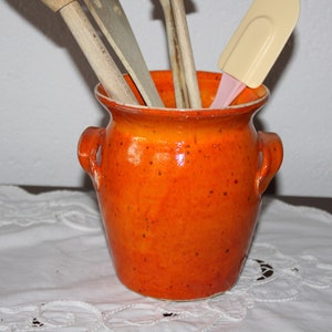 Könnte beinhalten: Orangener Keramik-Utensilienhalter mit gesprenkeltem Überzug. Der Halter hat zwei Griffe und ist mit Holzlöffeln und einem Spatel gefüllt.