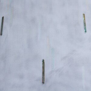 Peut inclure: Gros plan sur une surface de tissu blanc avec trois fines lignes verticales irisées.