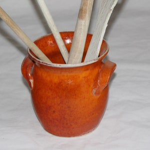 Könnte beinhalten: Ein brauner Keramik-Utensilienhalter mit zwei Griffen. Der Halter ist mit Holzlöffeln und -spateln gefüllt.