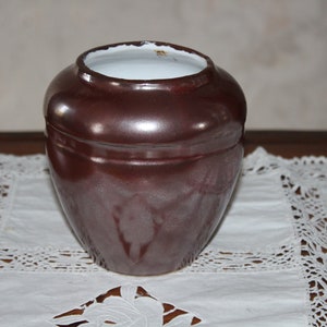 Peut inclure: Un vase en céramique brun avec un intérieur émaillé blanc. Le vase a une forme arrondie et une finition lisse et brillante.