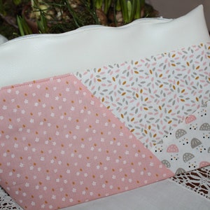 Könnte beinhalten: Eine weiße Reißverschlusstasche mit einem rosa-weißen Blumenmuster auf der einen Seite, einem weißen und rosa Blatt-Muster auf der anderen Seite und einem weißen und grauen Muster mit kleinen Kreisen auf der dritten Seite.