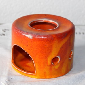 Könnte beinhalten: Orangener Keramik-Tee-Wärmer mit einem Loch oben und einer großen Öffnung an der Seite. Es gibt zwei kleine Löcher an der Seite.