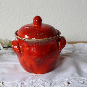 May include: A red ceramic pot with a lid and two handles. The pot has a speckled glaze and a brown rim.