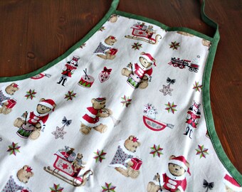 Può includere: Grembiule bianco con bordi e lacci verdi, con un motivo natalizio festivo. Il motivo include orsetti in abiti da Babbo Natale, trenini giocattolo, schiaccianoci e slitte, creando un tema festivo.