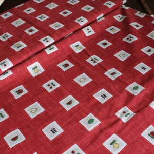 Könnte beinhalten: Roter Stoff mit einem sich wiederholenden weißen und grünen Muster aus Obst und Gemüse in Quadraten. Das Muster enthält Birnen, Wassermelonen, Trauben und Kirschen.