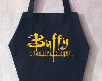 May include: Black tote bag featuring the text "Buffy the Vampire Slayer" in yellow, with a white cartoon zombie. The bag has black handles and a coffin-like shape.