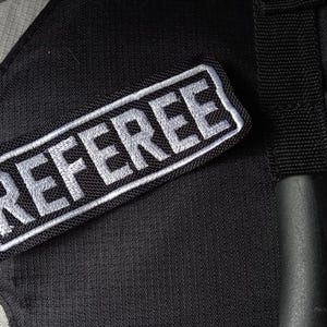 May include: A black fabric patch with white stitching that reads "REFEREE".