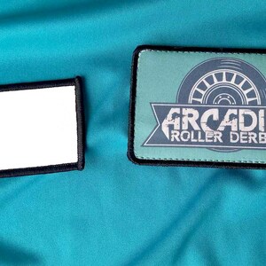 May include: Two rectangular patches with black stitching. The patch on the left is white. The patch on the right is green with a white graphic of a roller skate wheel and the text "ARCADIA ROLLER DERBY".