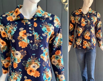 May include: A long-sleeved shirt with a navy blue background and a floral pattern in shades of orange, teal, and white. The shirt has a collared neckline and a button closure.
