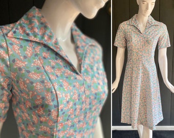 May include: A vintage dress with a floral print in shades of pink, blue, and green. The dress has a collared neckline, short sleeves, and a fitted bodice. It is a knee-length dress with a flared skirt.