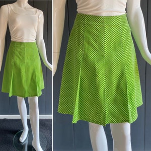 May include: A green mini skirt with white polka dots. The skirt has a pleated design and a straight hemline.