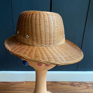 May include: A brown woven straw hat with a wide brim and a rounded crown. The hat has a few metal eyelets around the crown.