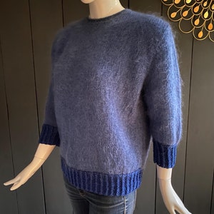 May include: A blue fuzzy sweater with a dark blue ribbed trim around the neck, cuffs, and hem.