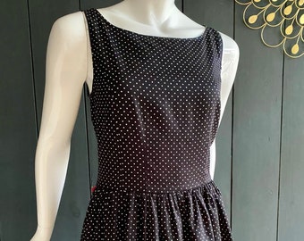 May include: A black sleeveless dress with white polka dots. The dress has a scoop neck and a fitted bodice. The skirt is full and flows out from the waist.