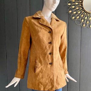 May include: A brown suede jacket with a collared neckline and button closure. The jacket features white stitching details and a slightly fitted silhouette.