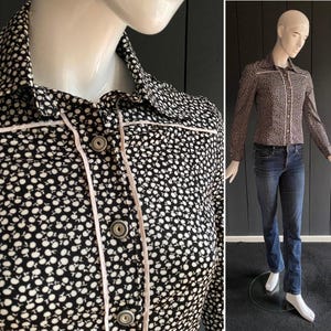 Peut inclure: Une chemise boutonnée à motifs noirs et blancs avec une bordure et des boutons rose clair. La chemise est associée à un jean bleu sur un mannequin. La chemise a un petit motif répétitif.