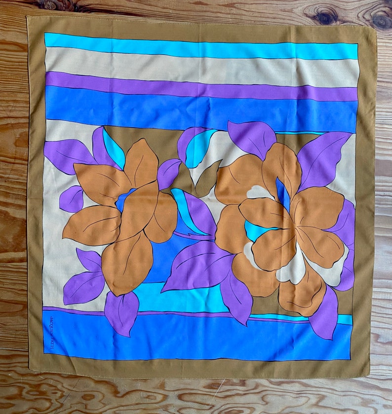 May include: A brown silk scarf with a colorful floral pattern. The pattern features large orange flowers with purple leaves and blue and white accents. The scarf has a striped border in shades of blue, purple, and beige.