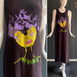 May include: A sleeveless, dark brown maxi dress featuring a colorful abstract face design. The face has yellow skin, pink lips, and purple hair. The dress is displayed on a mannequin.