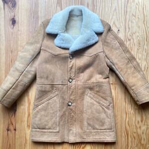 May include: A tan suede shearling coat with a large white shearling collar. The coat has a button closure and two large pockets.
