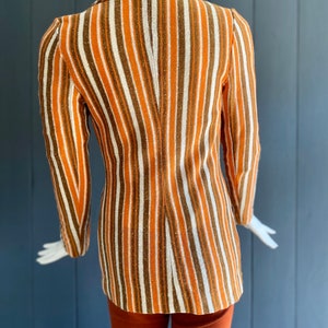 May include: A striped blazer with orange, brown, and white stripes. The blazer has a long sleeve and a classic collar.