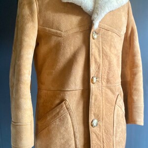May include: A brown suede jacket with a white shearling collar and button closure. The jacket has two flap pockets on the front and a single button on each cuff.