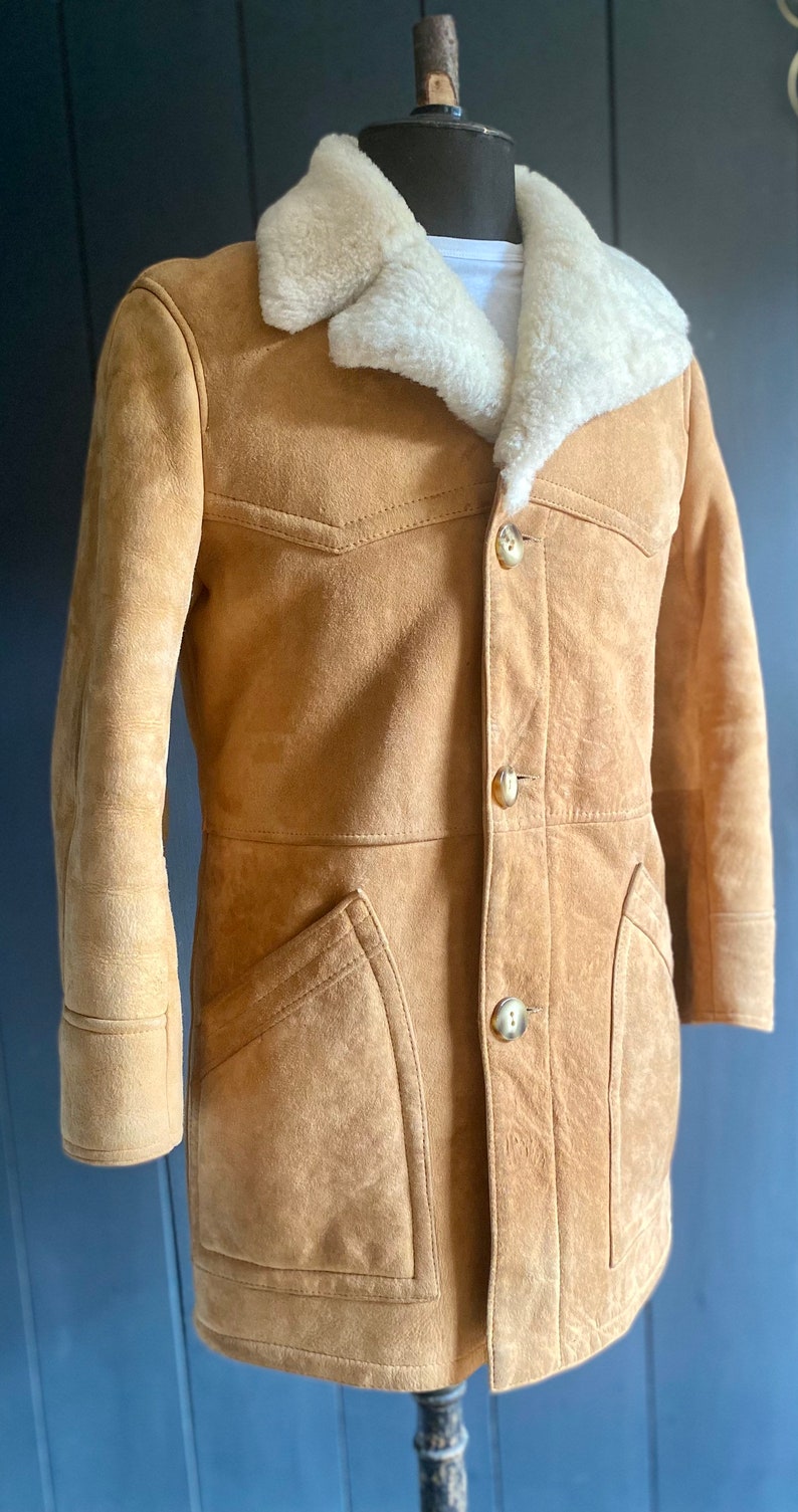May include: A brown suede jacket with a white shearling collar and button closure. The jacket has two flap pockets on the front and a single button on each cuff.