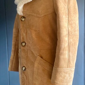 May include: A brown suede shearling coat with a white fur collar and a button closure. The coat has a patch pocket on the left side and a seam down the center of the back.