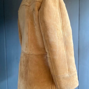 May include: A brown suede shearling coat with a white shearling collar. The coat has a long sleeve and a button closure.