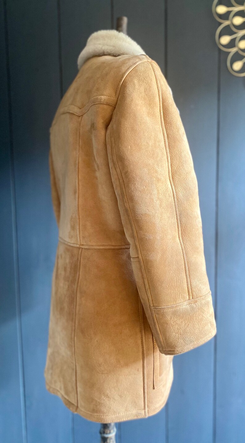 May include: A brown suede shearling coat with a white shearling collar. The coat has a long sleeve and a button closure.