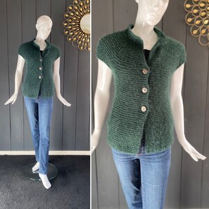 Op de afbeelding: Een donkergroene, korte, gebreide cardigan met knoopsluiting. De cardigan is gemaakt van een zacht, pluche materiaal.