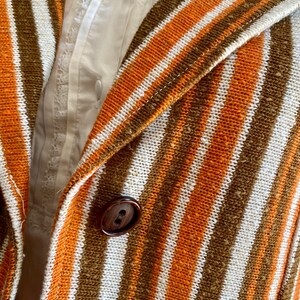 May include: Close-up of a striped fabric with orange, white, and brown stripes. A brown button is visible in the center of the image.
