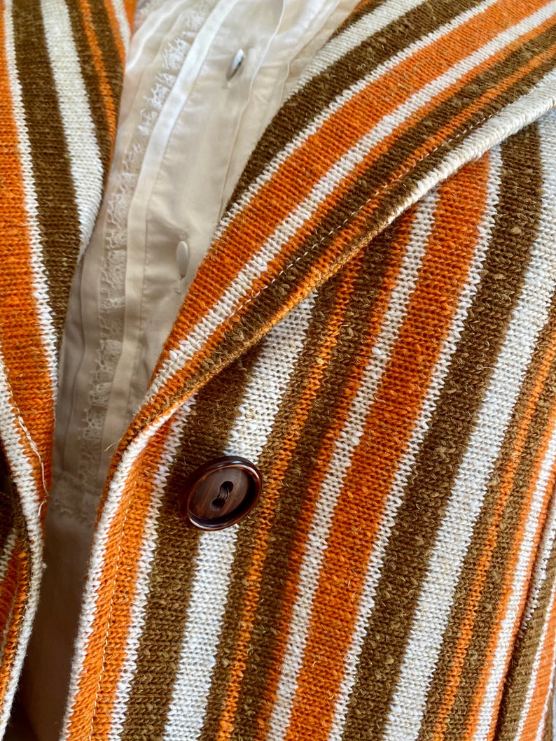 May include: Close-up of a striped fabric with orange, white, and brown stripes. A brown button is visible in the center of the image.