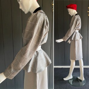 May include: A gray plaid peplum top with a fitted skirt. The top has a high neckline and long sleeves. The skirt is knee-length and has a straight silhouette.