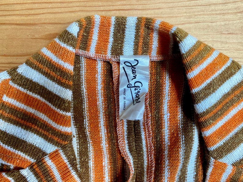 May include: A striped brown, orange, and white knit fabric with a white label that reads "Jean Girault Made in France".