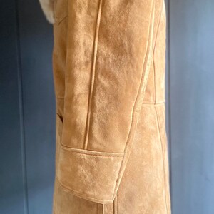May include: A brown suede shearling coat with a white shearling collar. The coat has a long length and a classic design.