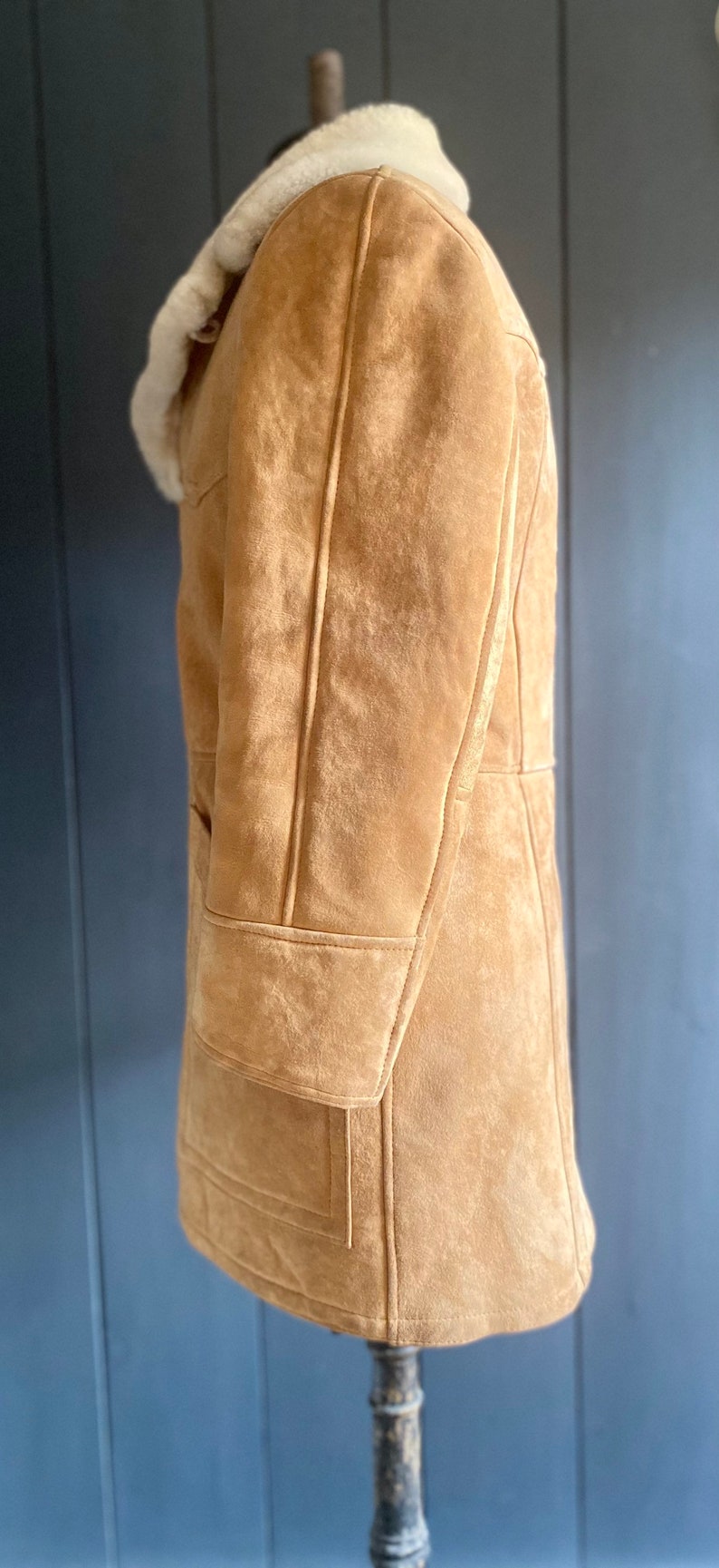 May include: A brown suede shearling coat with a white shearling collar. The coat has a long length and a classic design.