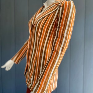 May include: A striped blazer with brown, orange, and white stripes. The blazer has a notched collar and long sleeves.