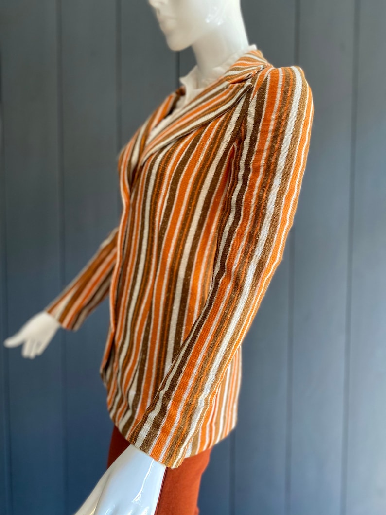 May include: A striped blazer with brown, orange, and white stripes. The blazer has a notched collar and long sleeves.