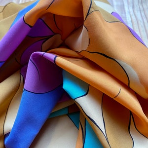 May include: A colorful silk scarf with a geometric pattern in shades of orange, purple, blue, and white.