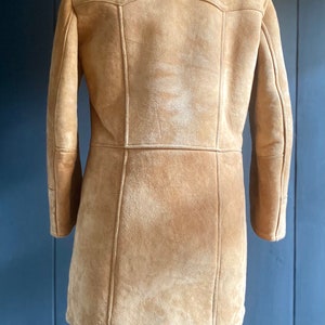 May include: A brown suede jacket with a shearling collar. The jacket has a long, fitted silhouette and is lined with a soft, warm fabric.