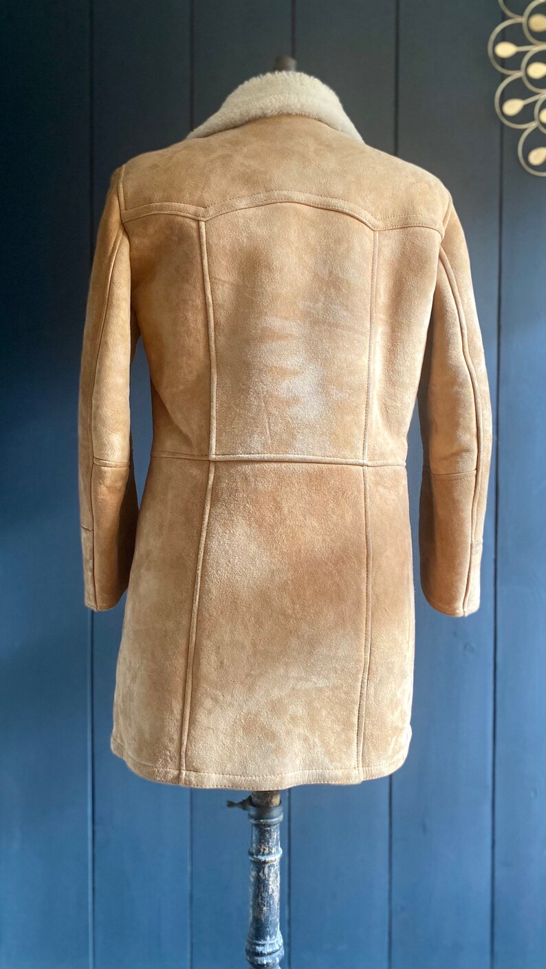 May include: A brown suede jacket with a shearling collar. The jacket has a long, fitted silhouette and is lined with a soft, warm fabric.