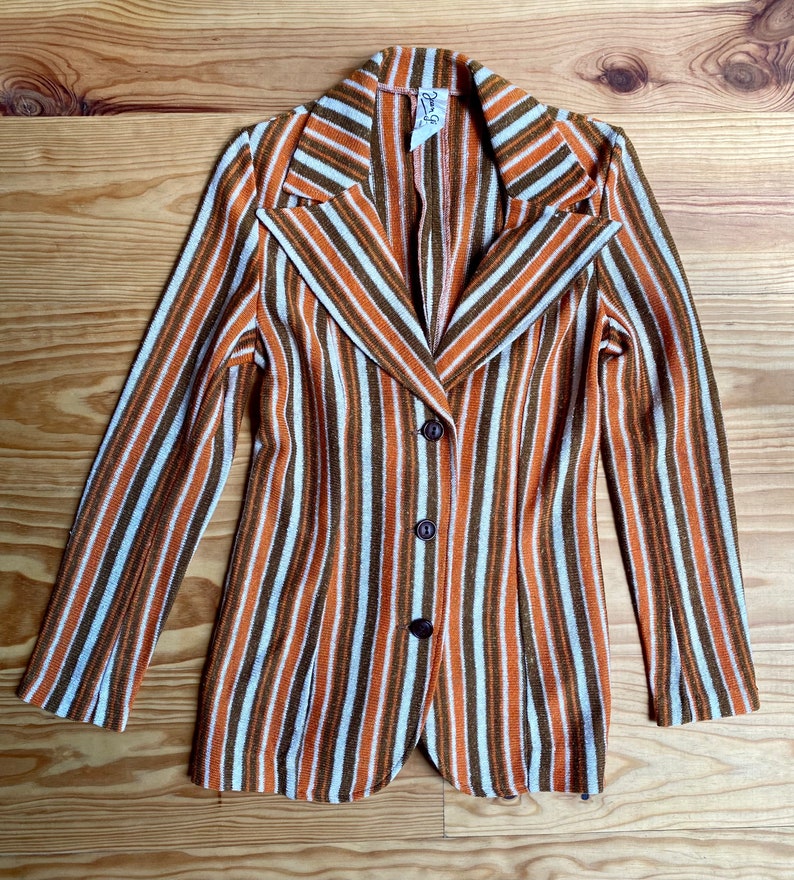 May include: A striped blazer with a brown, white, and orange color scheme. The blazer has a notched collar, long sleeves, and three buttons down the front.