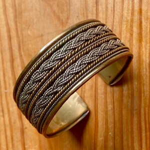 Peut inclure: Un bracelet jonc tressé en argent et or avec un motif tissé.